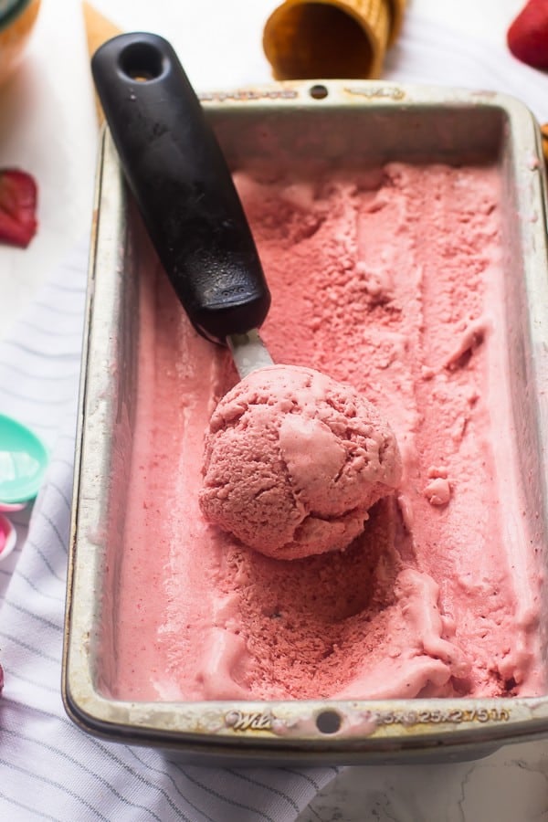 Strawberry coconut ice cream in a tub with a scoop. 