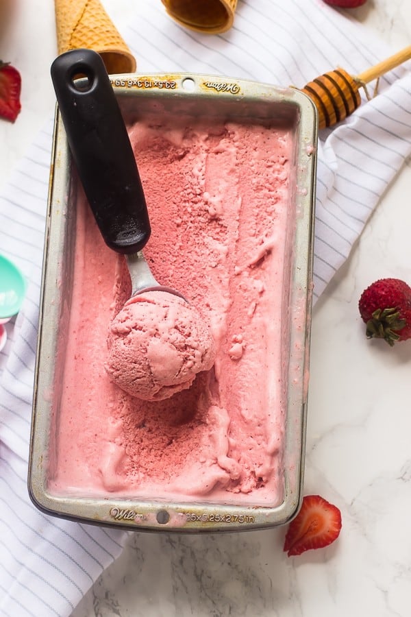 A tub of vegan strawberry coconut ice cream in a tub with a scoop.