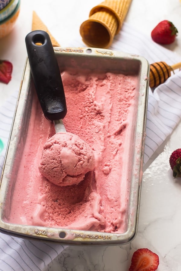 A big tub of vegan strawberry coconut ice cream with a scoop on top.