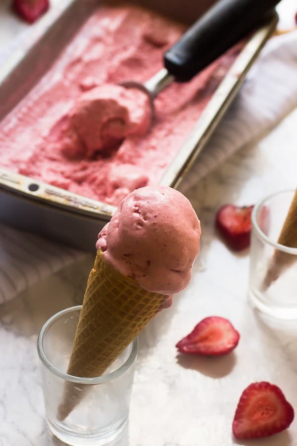 Vegan strawberry coconut ice cream in a cone with sliced strawberries in the background. 