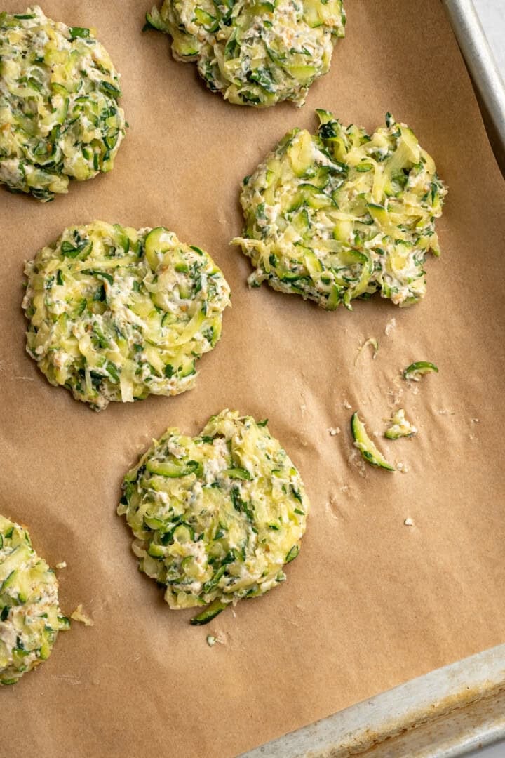 Shaped zucchini fritters on parchment lined baking sheet. - 4