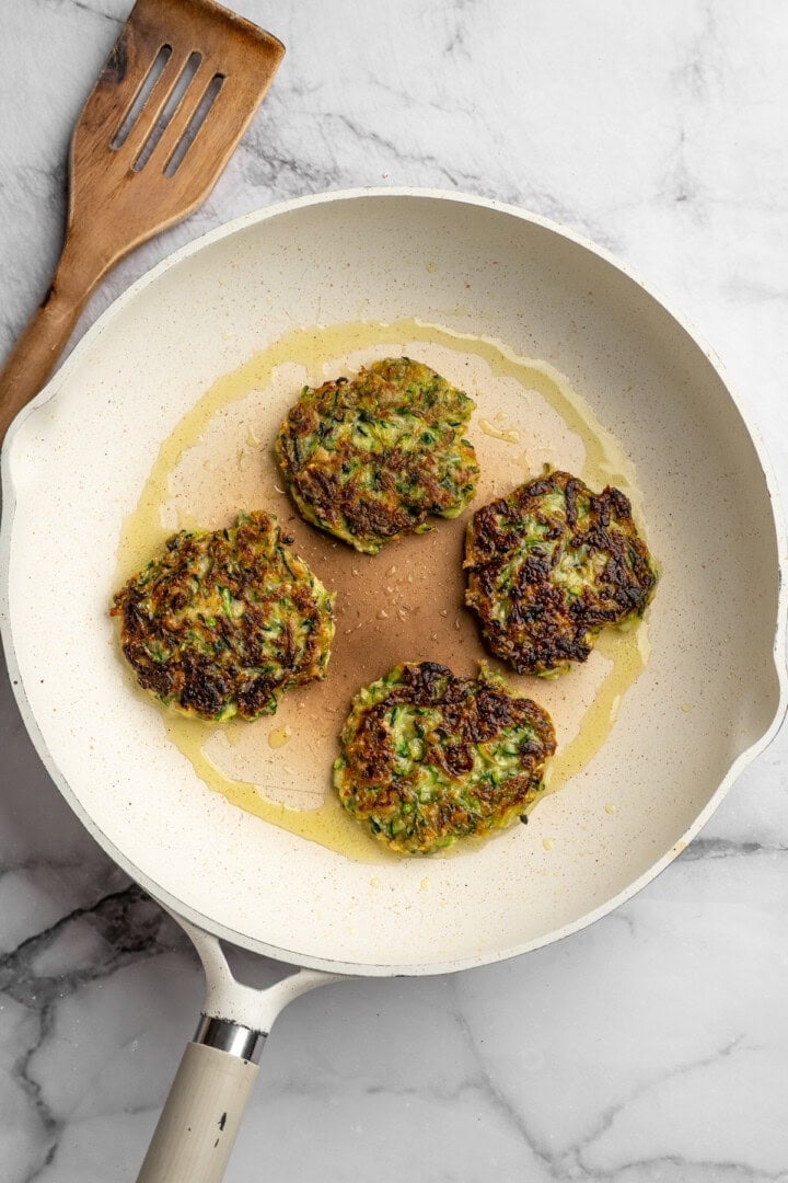 Made with coconut flour, these crispy zucchini fritters are gluten-free and vegan! They're easy to make, perfect for a side or appetizer. Zucchini fritters in skillet with oil.