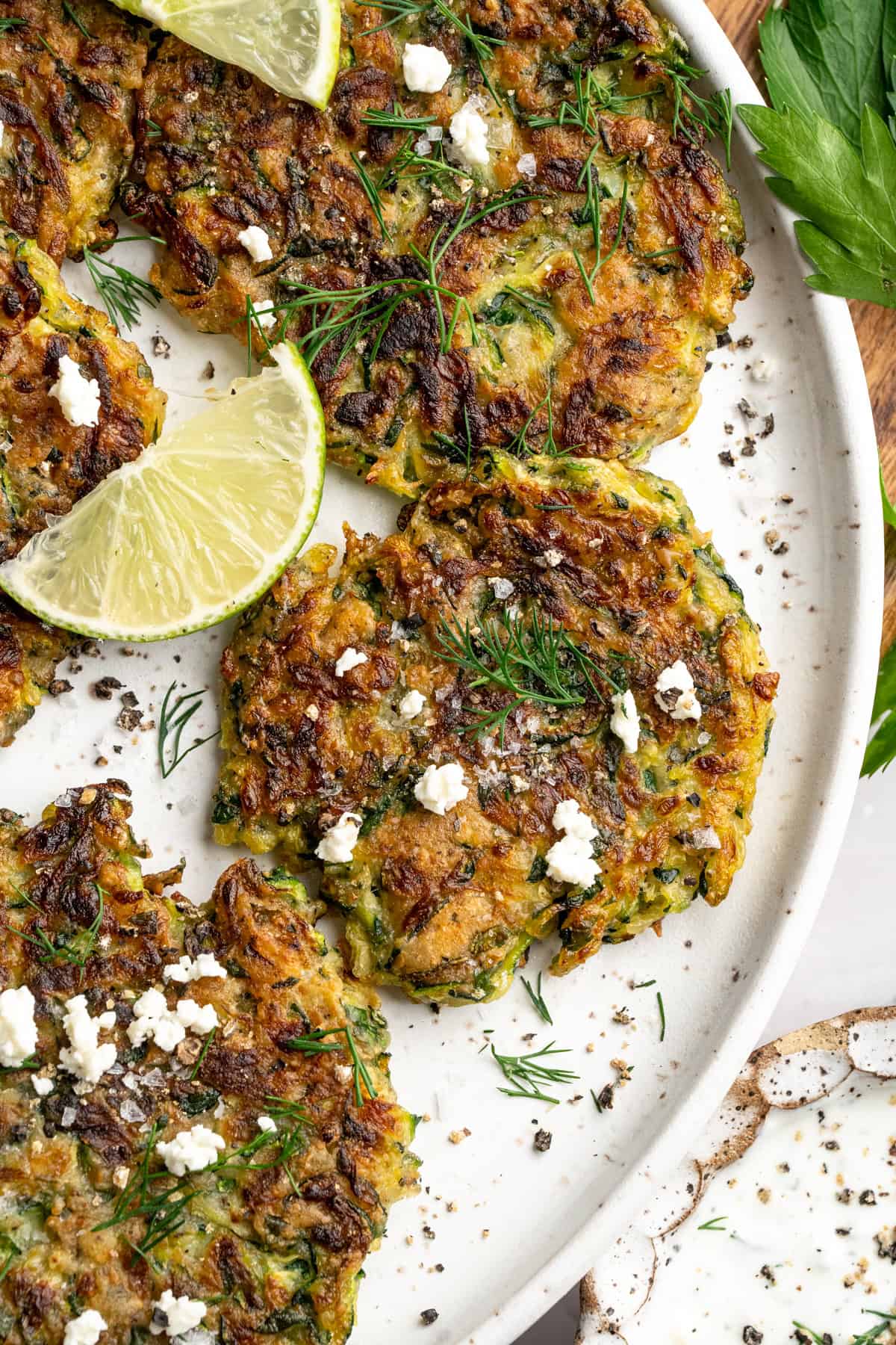Gluten-free zucchini fritters on platter topped with dill and vegan feta. - 5