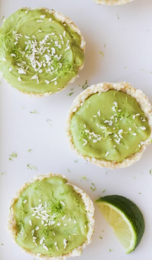 Top down shot of no bake vegan key lime tarts on a white table with a wedge of lime. 