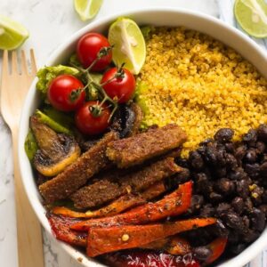 Top down shot of vegan fajita bowl on a white table with a wood spoon.