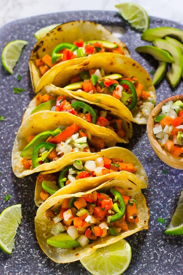 Top down shot of vegan sweet potato tacos with wedges of lime. 