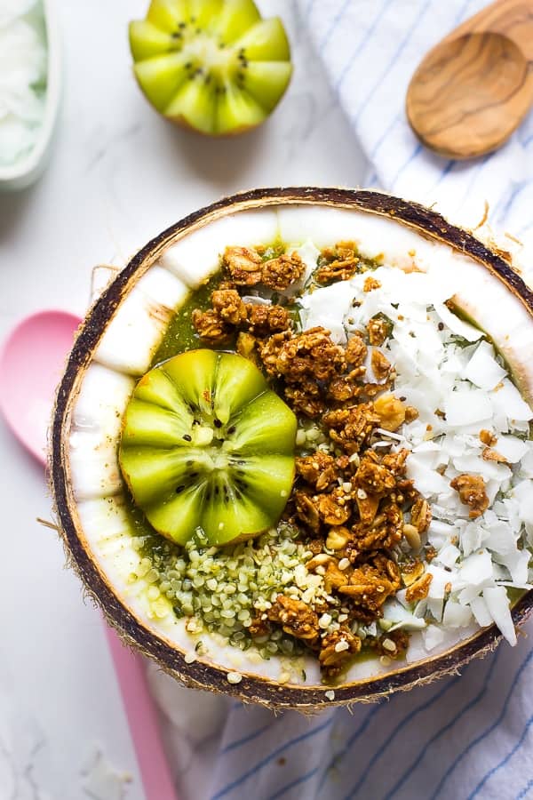 Overhead shot of coconut flakes kiwi and granola in coconut half. 