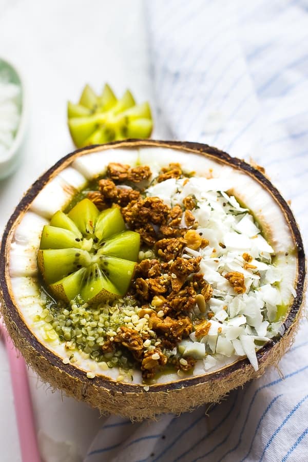 A coconut kiwi green smoothie bowl in half a coconut.