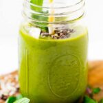 Mint chocolate chip green smoothie in a mason jar with a straw and sprig of mint.