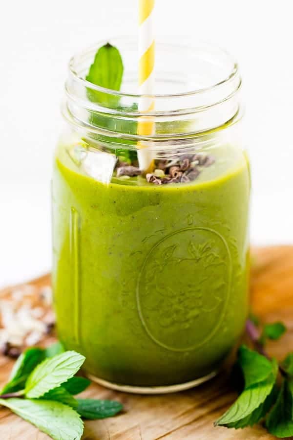 A mint chocolate chip green smoothie in a mason jar on a wood table. 