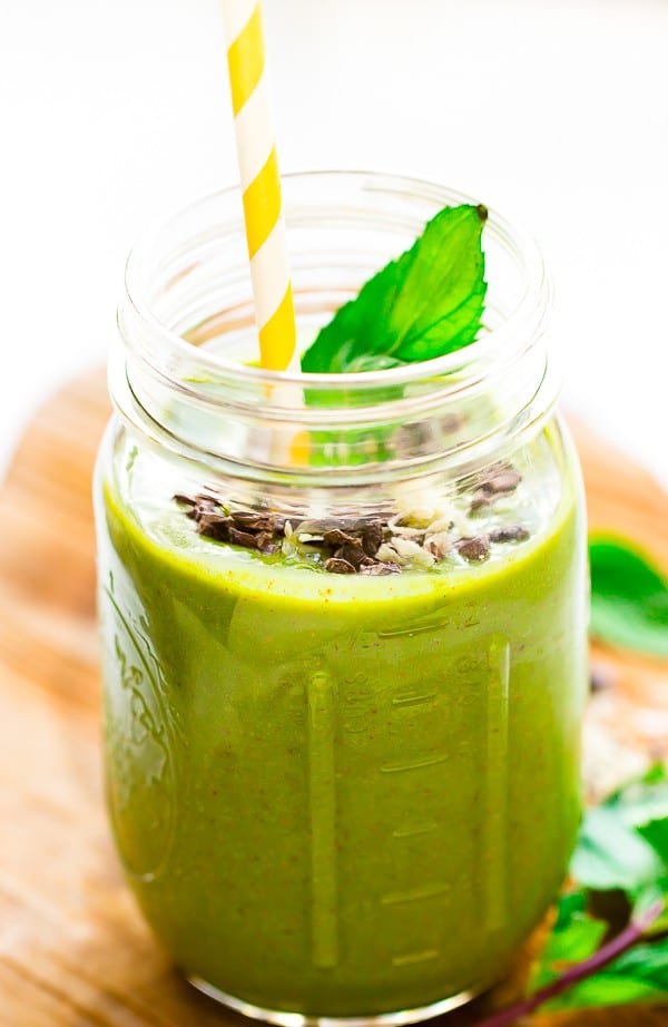 A mint chocolate chip green smoothie in a mason jar with a yellow straw. 