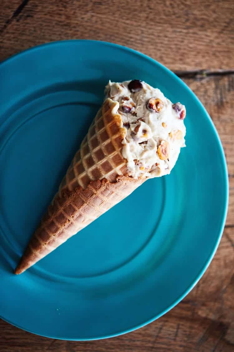 Whiskey hazelnut no churn ice cream in a waffle cone on a blue plate.