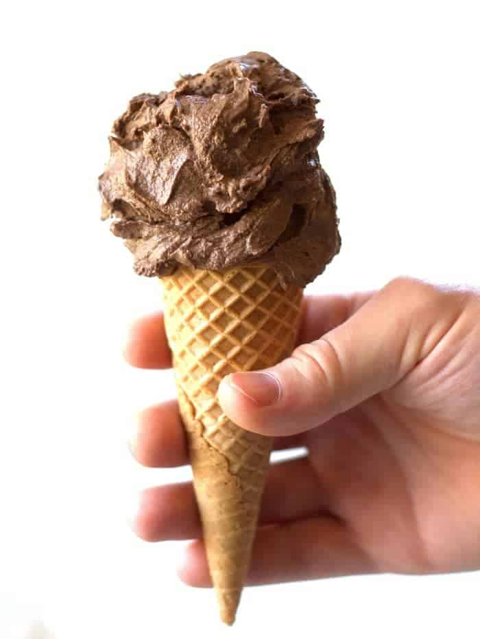 Hand holding vegan chocolate ice cream in a cone.