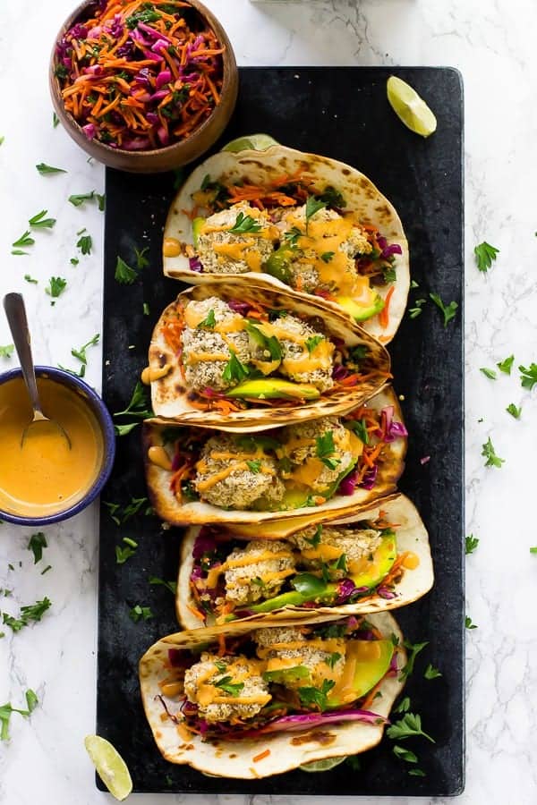 Overhead shot of cauliflower tacos on a black slat with sauce and slaw on the side. 