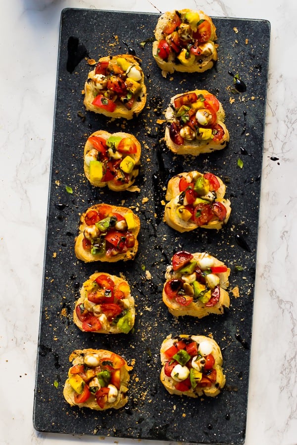 Top down shot of avocado caprese bruschetta on a grey slate. 