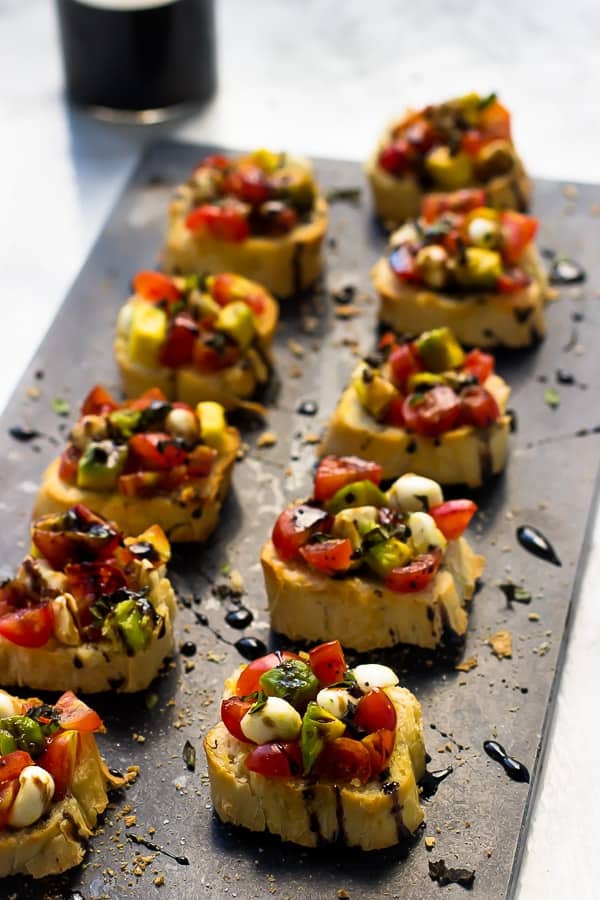 Rows of bruschetta drizzled with a balsamic reduction on a grey slate.