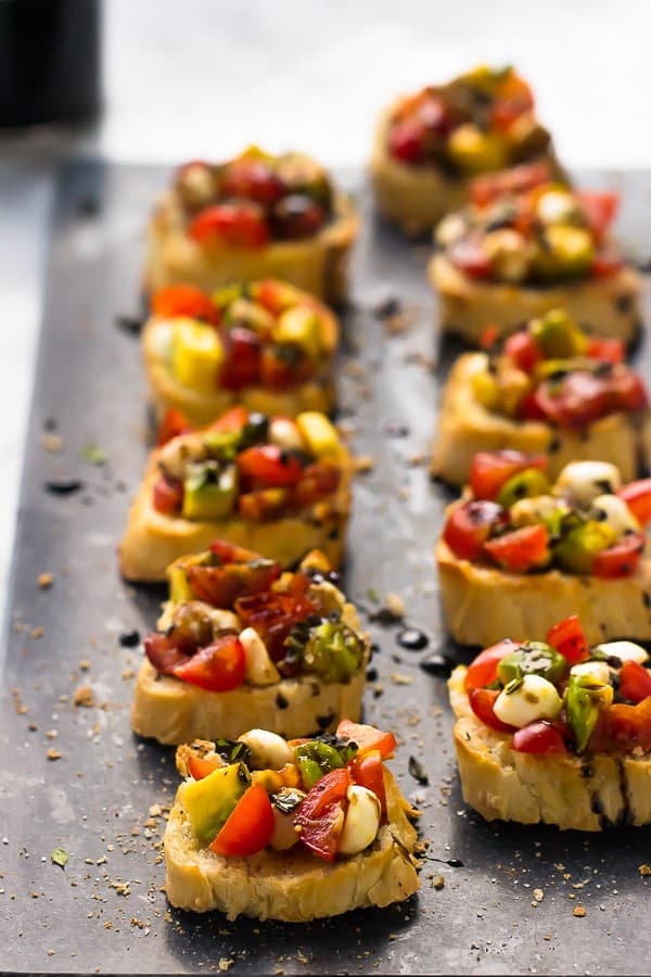 Rows of avocado caprese bruschetta topped on a grey slate.