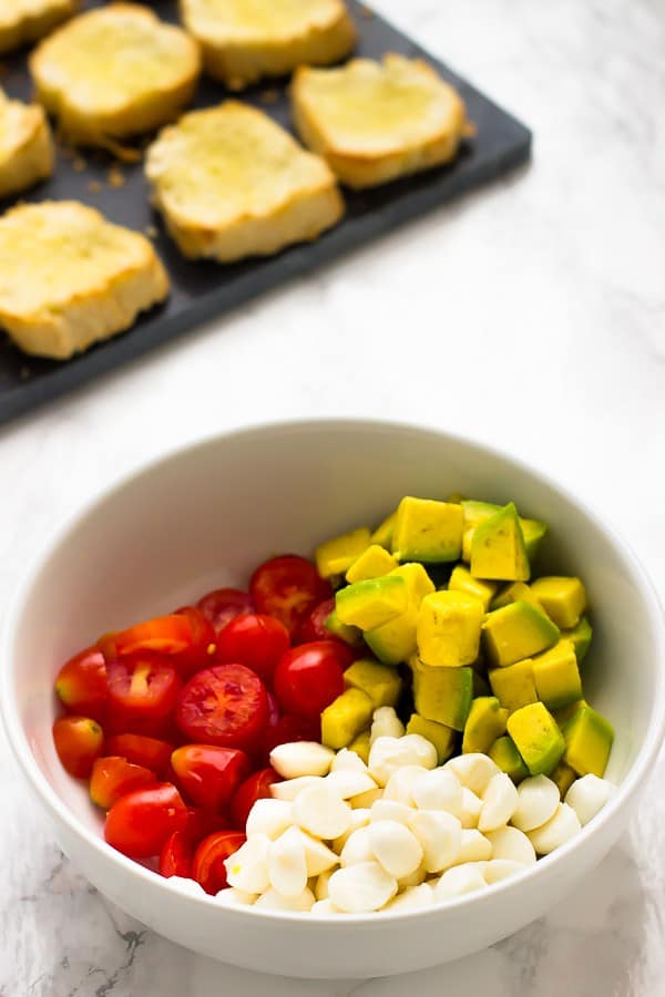 A white bowl containing diced avocado garlic and tomatoes. 