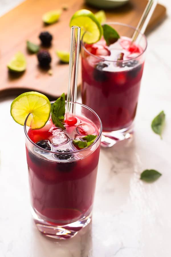 Two glasses of blackberry limeade, garnished with lime. 
