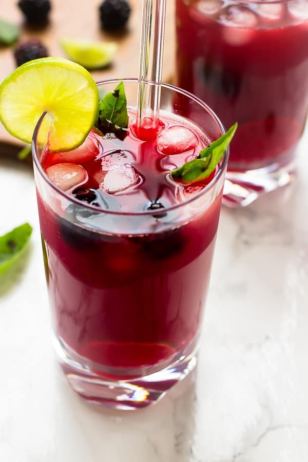 Close up of blackberry limeade in a glass with a straw. 