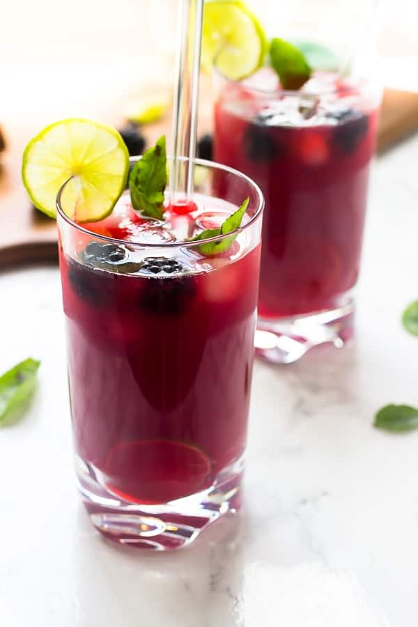 Two glasses of blackberry limeade with slices of lime. 