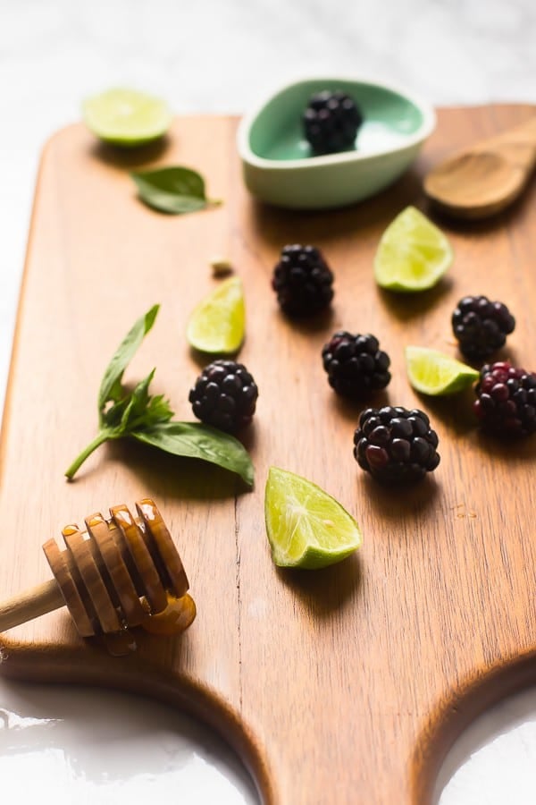 Blackberries lime wedges and honey on a chopping board.