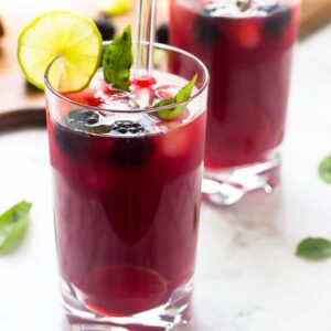 Side shot of two glasses of blackberry limeade with straws.