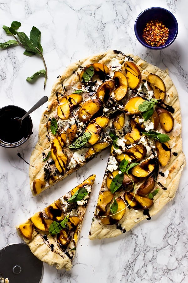 Top down shot of grilled peach pizza with a slice cut out. 