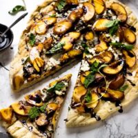Top down shot of grilled peach pizza on a marble counter.