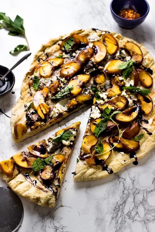 Top down shot of grilled peach, basil and goat cheese pizza with a slice taken out. 