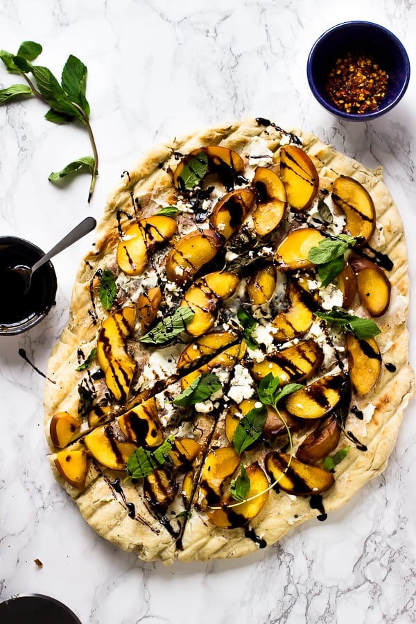 Overhead shot of grilled peach, basil and goat cheese pizza on a marble tabletop. 