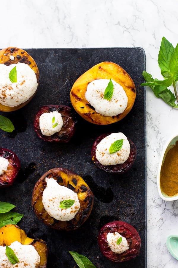 Overhead shot of grilled fruit topped with coconut cream on a grey slate. 