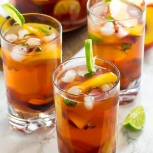 Glasses full of stone fruit sangria on a white table.