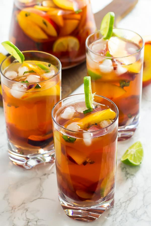 Three glasses of stone fruit sangria in front of a pitcher of sangria. 