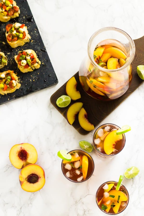 Top down shot of peach stone fruit sangria in a pitcher and in glasses with bruschetta on the side. 