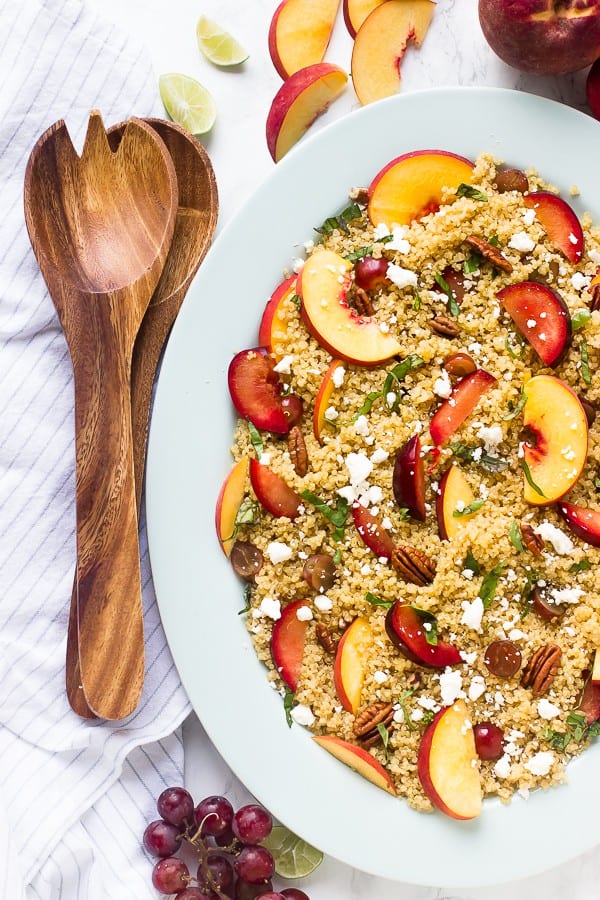 Quinoa stone fruit salad on a white dish with a wooden spoon on the side. 