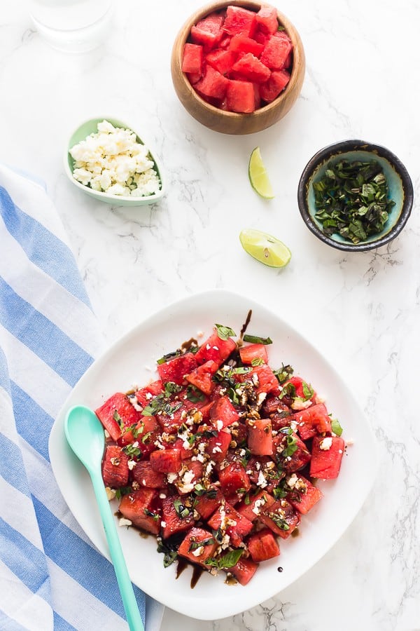 Overhead shot of watermelon feta salad on a white dish with a bowl of cubed watermelon on the side. 