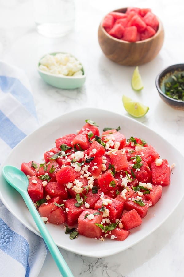 Watermelon feta salad on a white dish with a blue spoon on the side. 