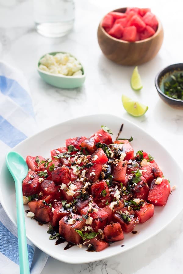 Watermelon feta salad on a square white plate with a blue spoon on the side. 