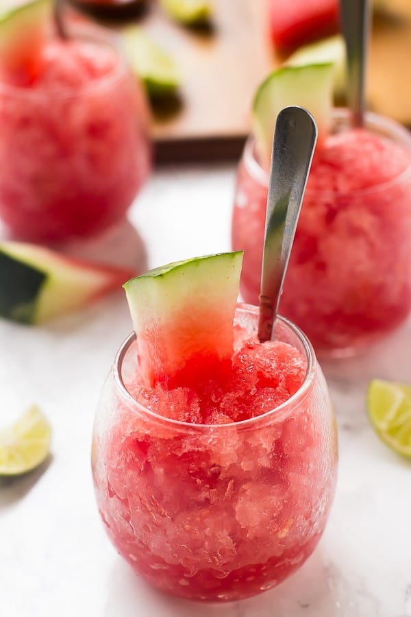 Three round glasses of watermelon granita with spoons in them. 