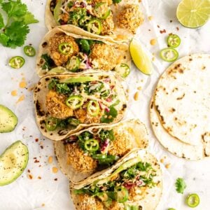 Crispy cauliflower tacos on a marble slab surrounded by garnishes and tortillas