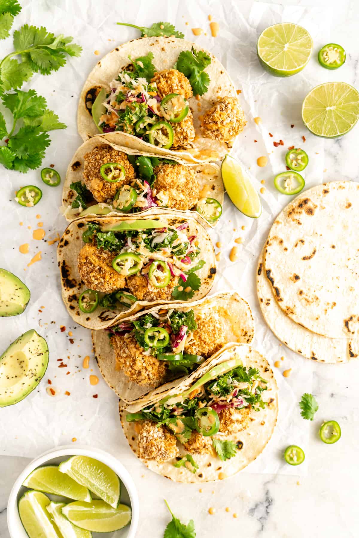 Overhead view of line of folded Crispy Cauliflower Tacos, surrounded by garnishes