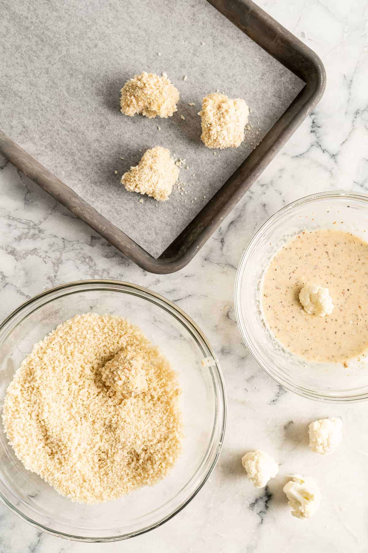 Cauliflower being dipped in bowls of batter and breadcrumbs, then placed on baking sheet