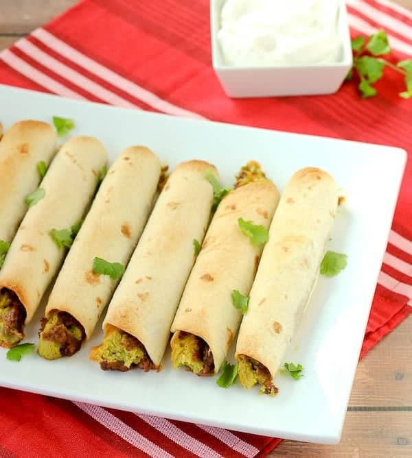 A row of vegetarian baked taquitos on a square white dish.