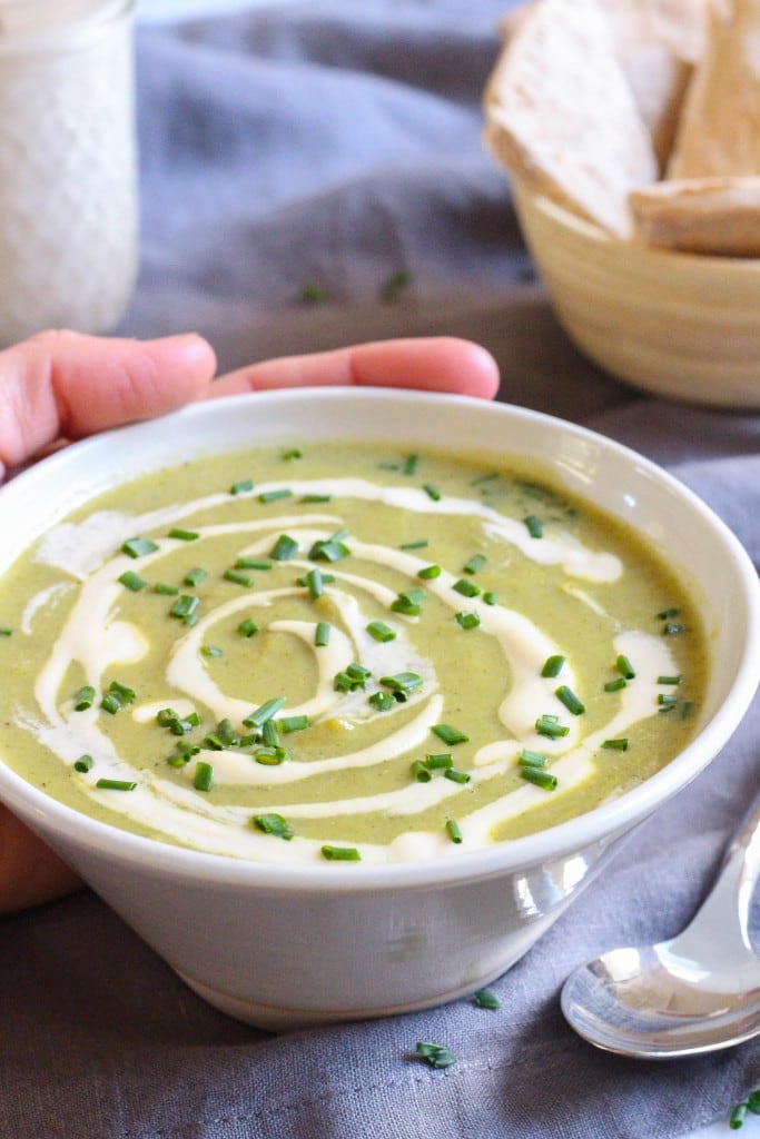Hand cradling a white bowl of broccoli soup in a white bowl.