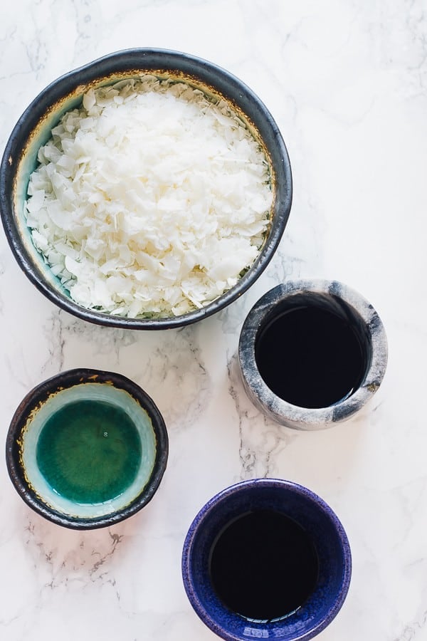 Overhead shot of a bowl of coconut flakes, a bowl of tamari, a bowl of liquid smoke, and a bowl of maple syrup