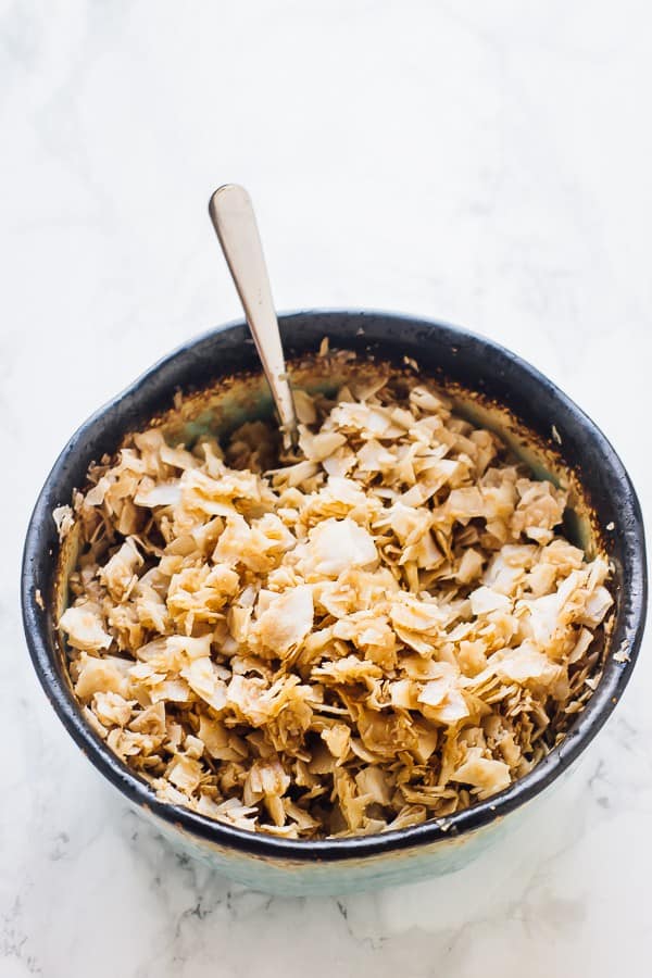 A bowl of coconut flakes seasoned with tamari, liquid smoke, and maple syrup, with a spoon