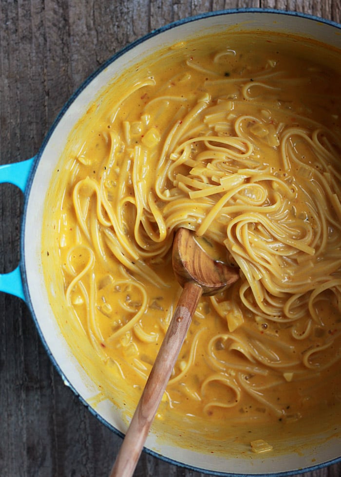 Wooden spoon stirring  creamy pumpkin pasta in a blue pot. 
