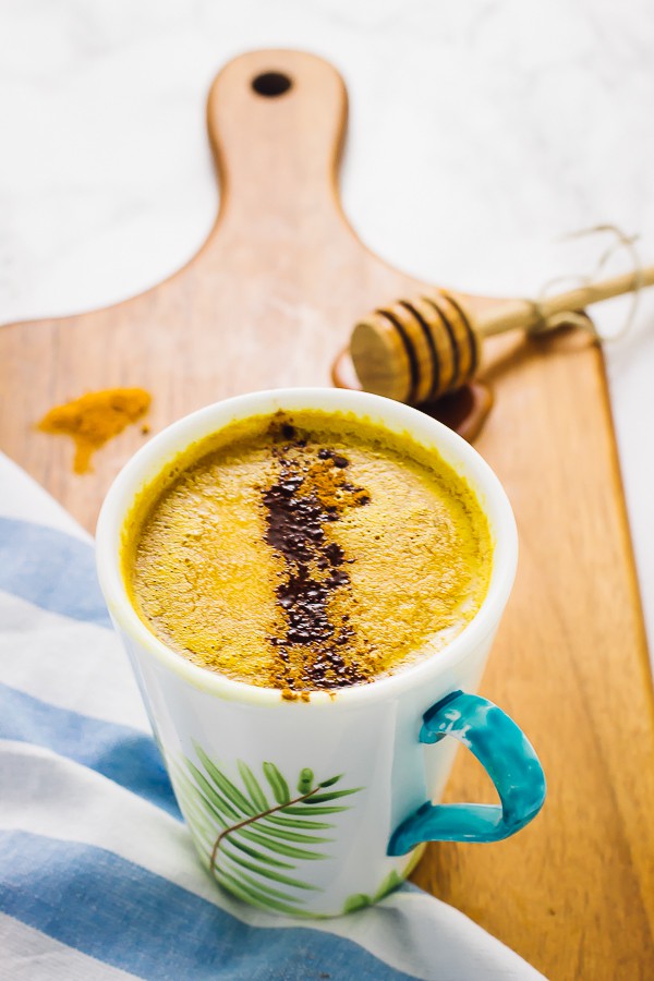 Pumpkin spice golden milk in a white mug, on a wood board.