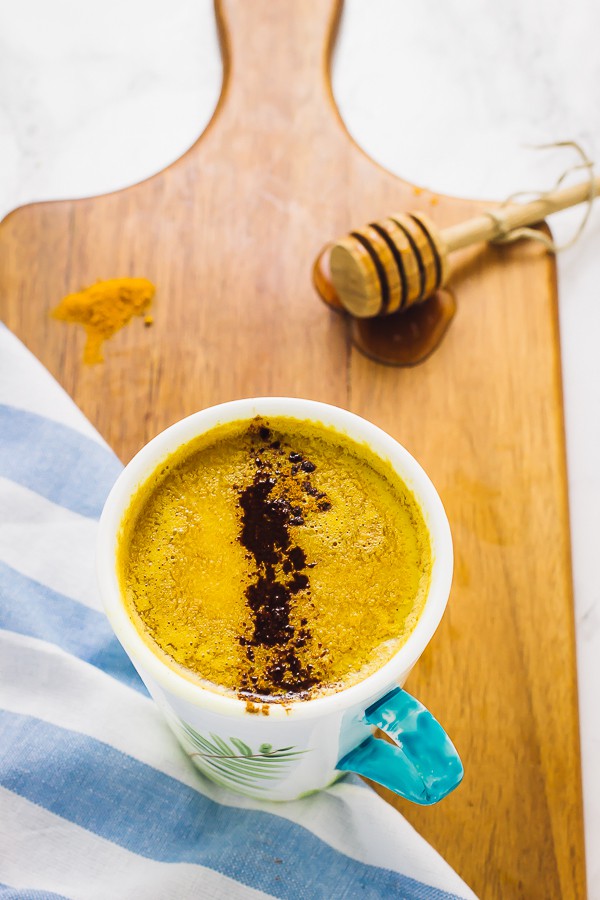 Overhead shot of pumpkin golden milk in a white and blue mug on a wooden board.